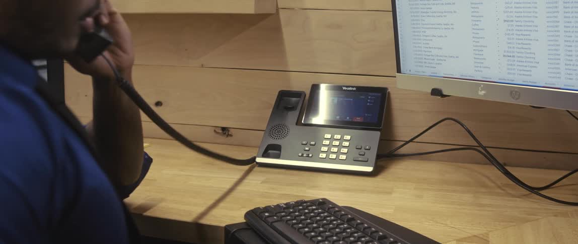 A man at a desk in an office answers the phone and speaks briefly