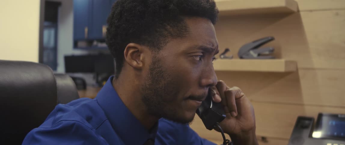 Businessman wearing a blue shirt and a black tie talks on the phone at the office
