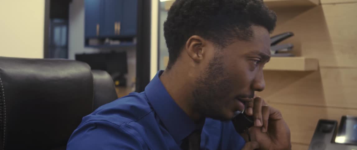Male office worker leaning back during a phone call sits upright and smiles then looks upset