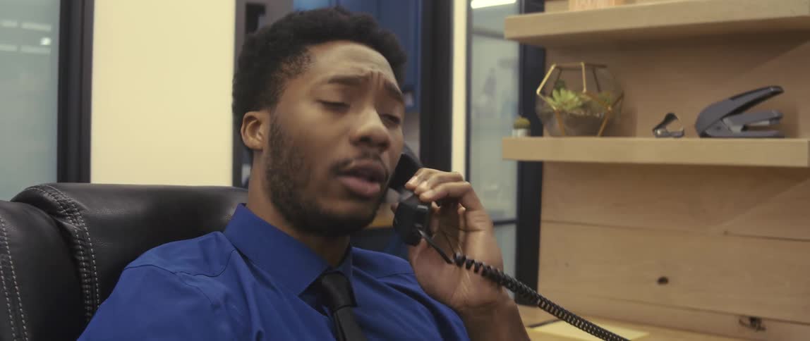 A black male employee talks on a phone and suddenly looks extremely worried
