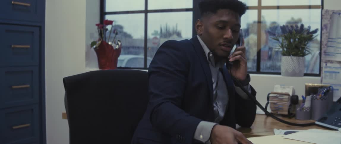 A busy office employee goes through files while talking on a phone