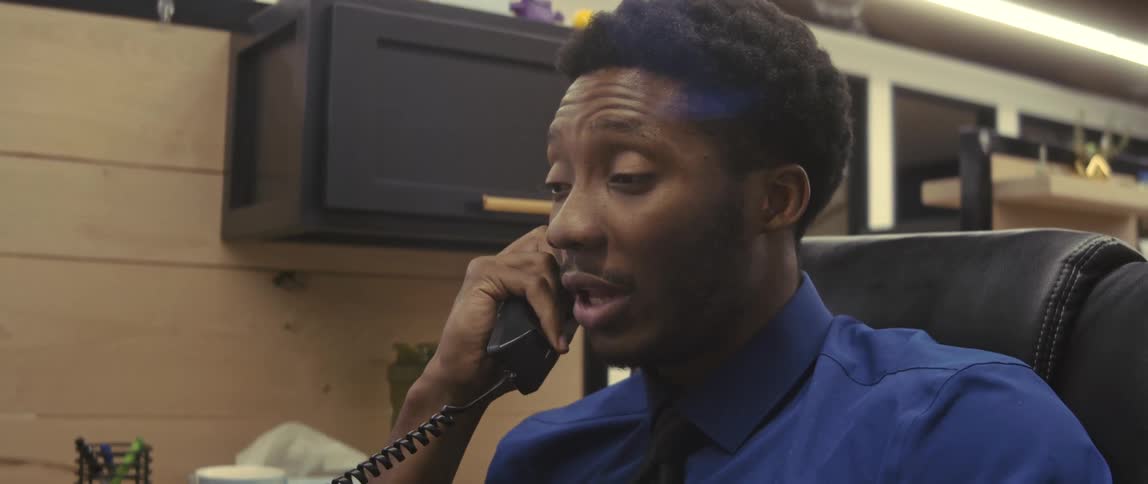 A happy office worker wearing a blue shirt talking on the phone on his cubicle