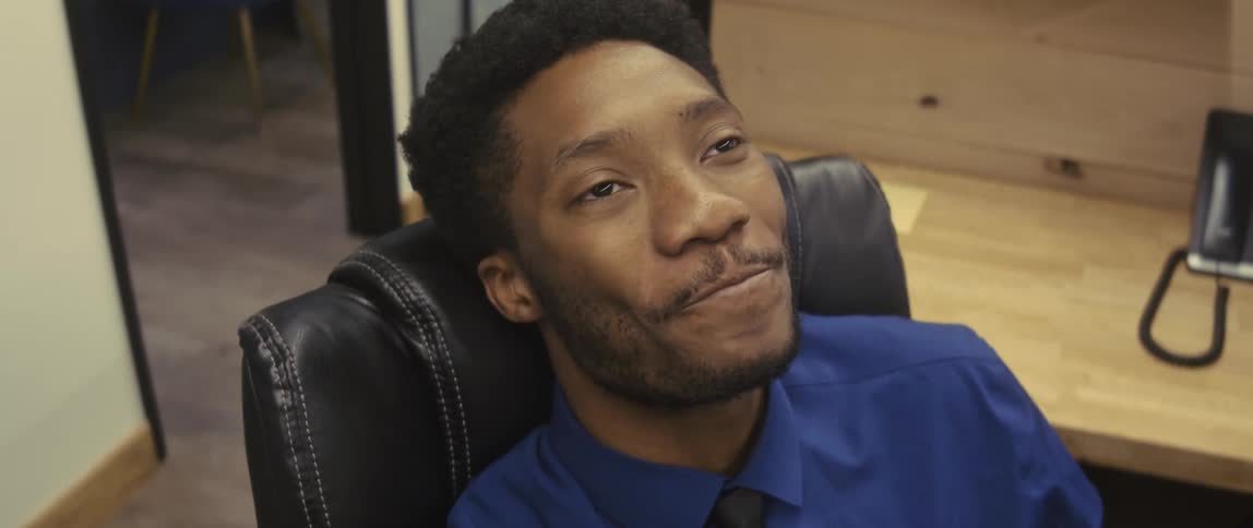 Overjoyed businessman dressed in a blue shirt and black tie sits in a chair at the office