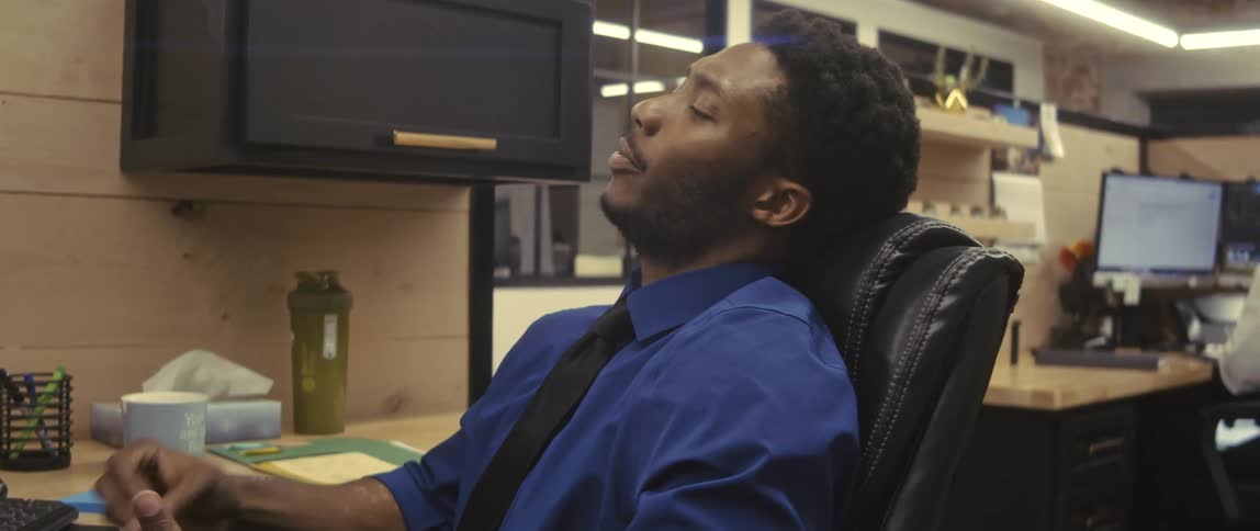 A man in blue business suit and tie is sitting on a black chair and is huffing and puffing exhaustion