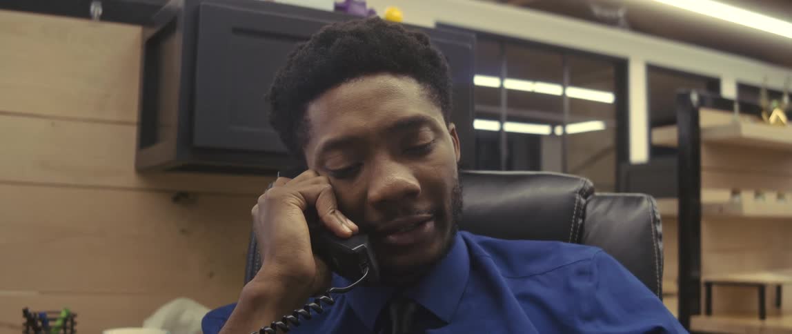 An office worker wearing a blue shirt talking on the phone in his cubicle