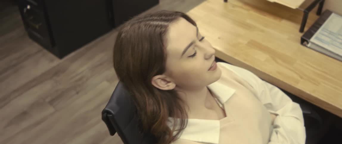 A white female employee types on a keyboard before leaning back in her chair and looking up