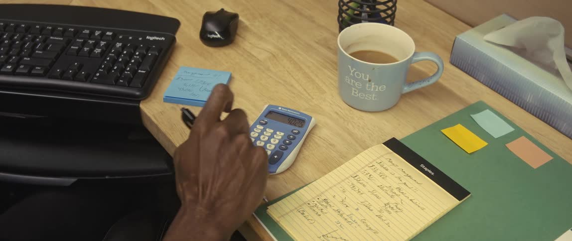 Hands of a man at an office desk typing on a calculator