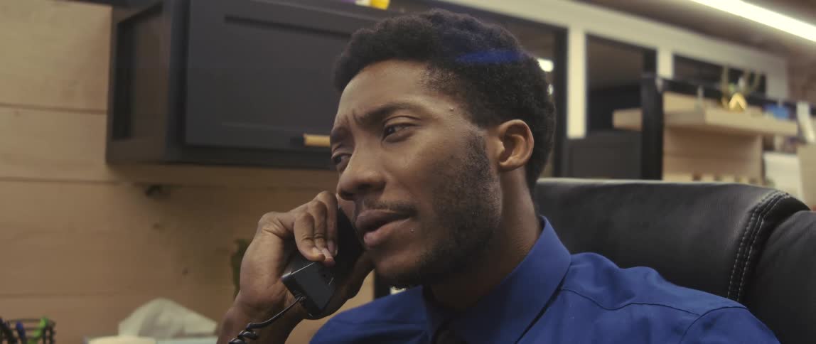 A concerned office worker wearing a blue shirt talking on the phone in his cubicle