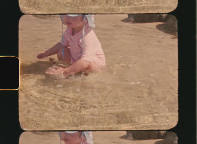 Super 8 film of a child in light colored clothing playing with water at the beach