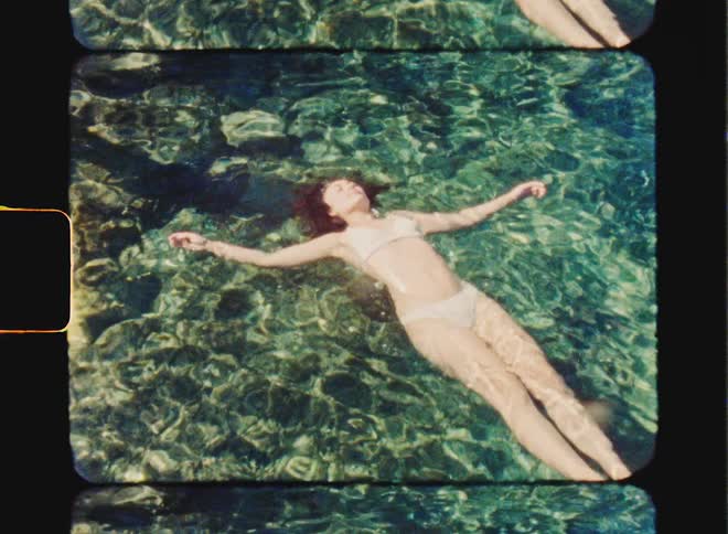 Super 8 film of a woman in a bikini, she is floating in the sea on a sunny day