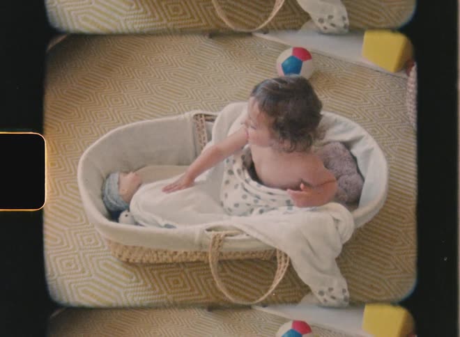 Super 8 film of a child playing, she is sitting inside a crib with her doll