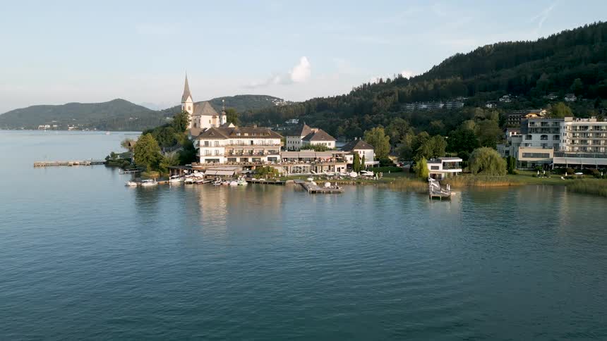 A picturesque lakeside resort with a church buildings and boats surrounded by lush greenery and mountains