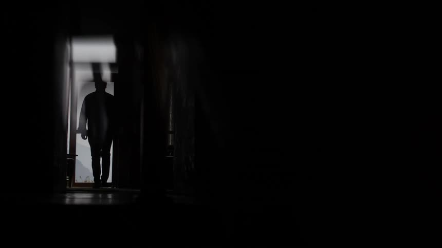 Man walking through a dimly lit building is silhouetted by sunlight from an open door