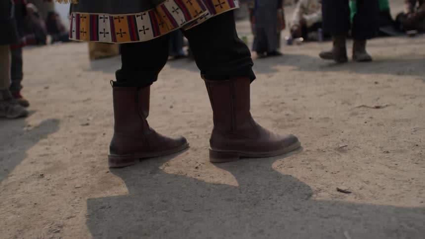 Close up of a persons legs in brown leather boots on dry ground
