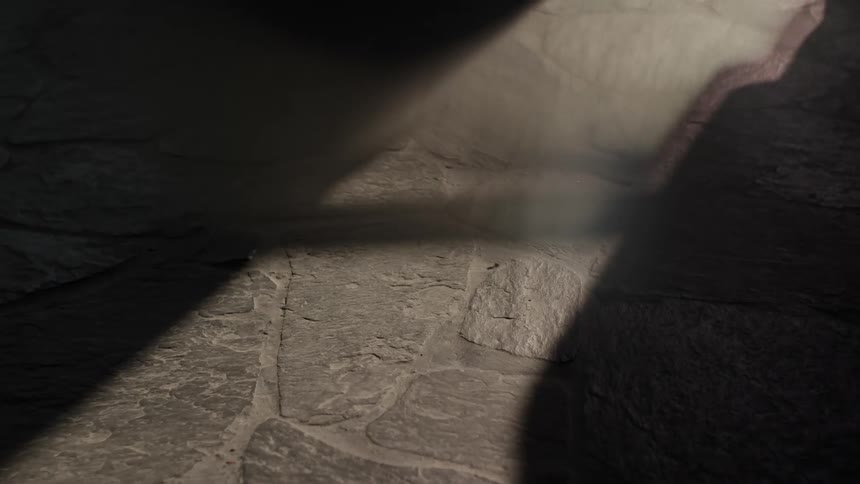 A floor made of stones and there is a shadow passing through a beam of natural light that is on the floor