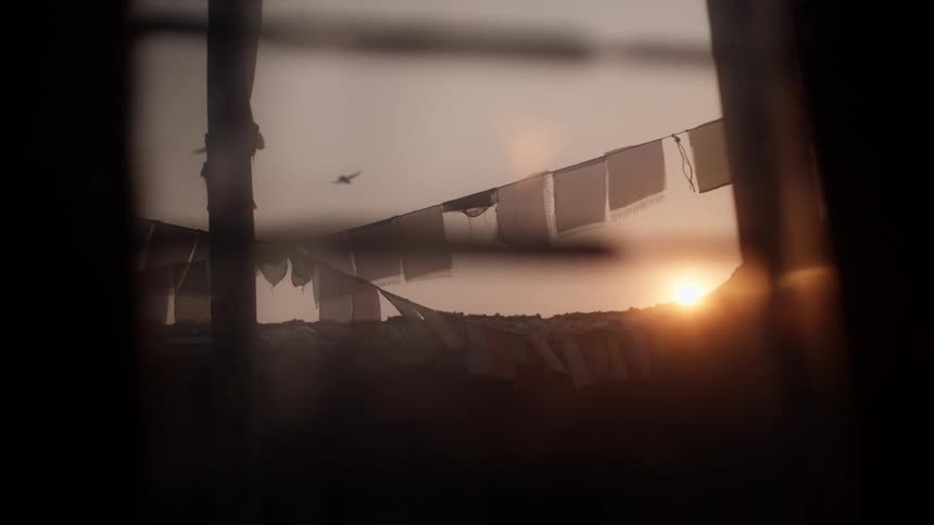 A string of flags possibly prayer flags against a setting or rising sun with warm hues