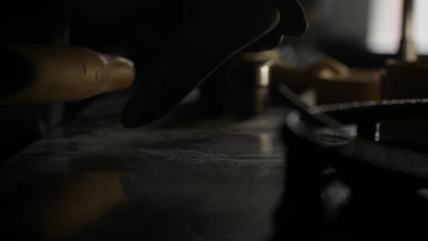 Hands of a person holding a wooden rolling pin and dough on the table