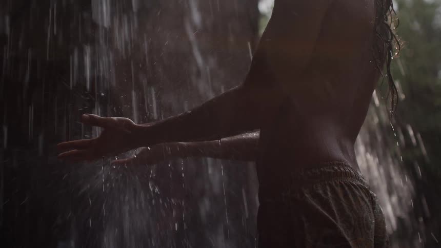 A person standing under a waterfall with their hand outstretched to catch water droplets