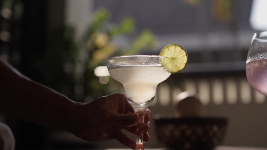 A mans hand grabs a martini off of a table on a balcony at night