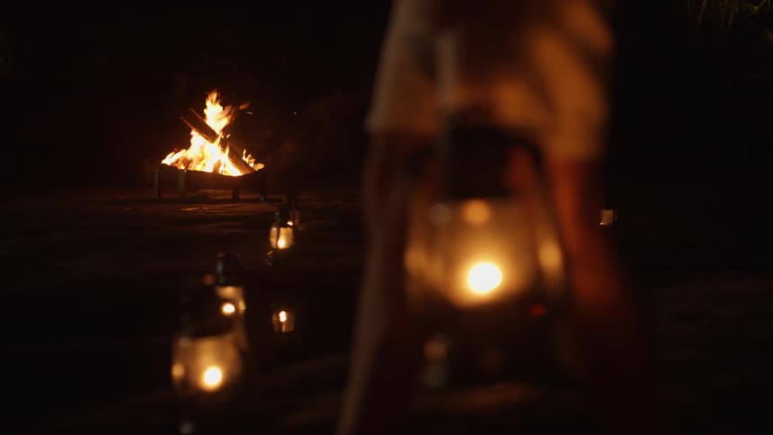 A man in shorts carries a lantern in a nighttime scene where lanterns softly illuminate the ground