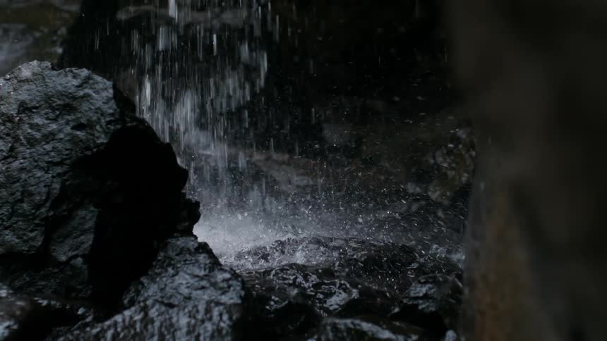 The bottom of a waterfall crashes onto some very large black rocks