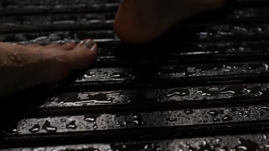 A mans feet are shown barefoot taking one slow step on a wooden deck in the rain