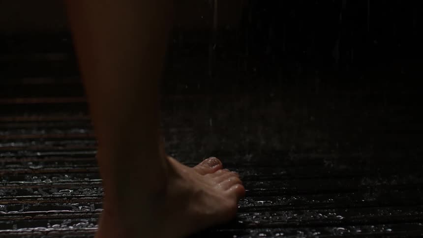 A woman walks barefoot into a shower