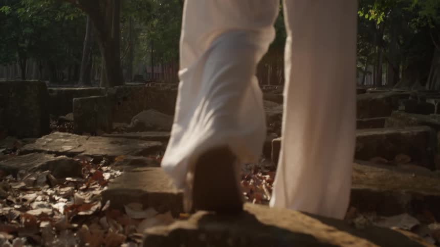 Person wearing white pants steps upon uneven stone blocks in the woods