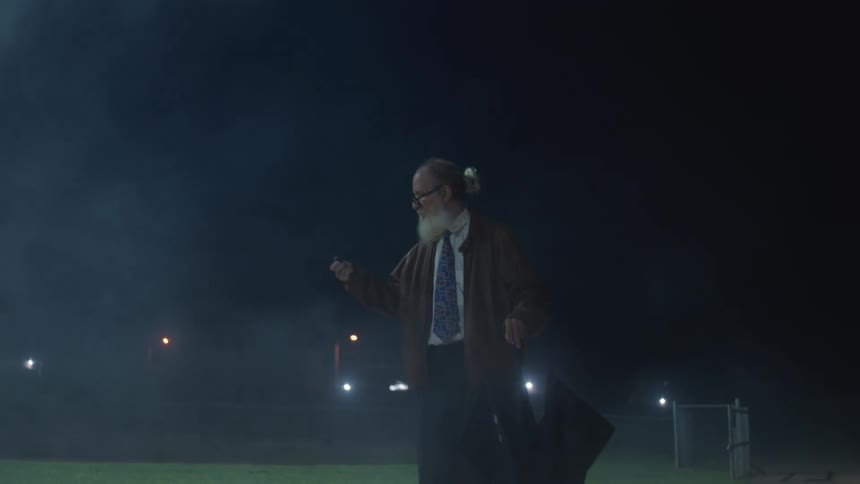 Older coach uses a stopwatch to time an athlete running on the track at night