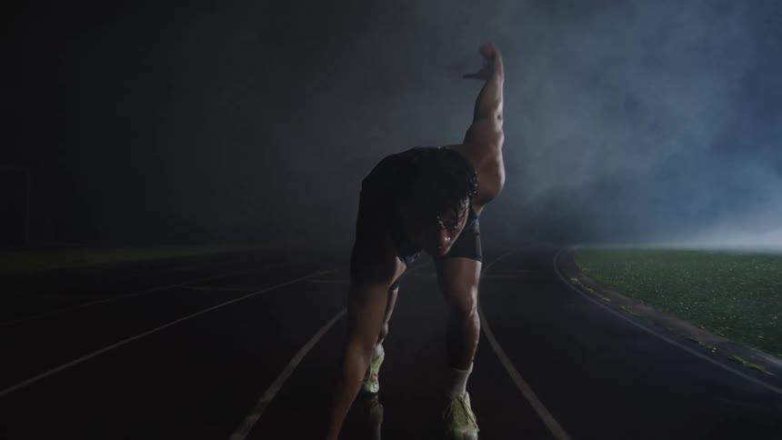 Man in running stance in long shot on a wet night running track