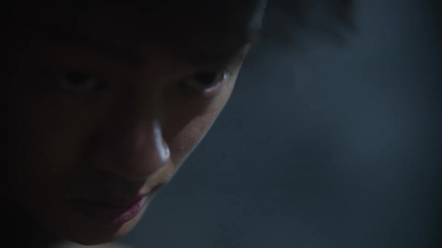 The face of a man staring straight ahead in a dark environment