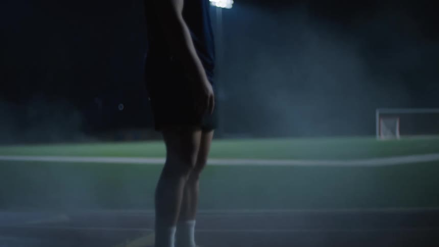 A man in a blue tank top is standing on a red running track in an outdoor setting at night illuminated by spotlights