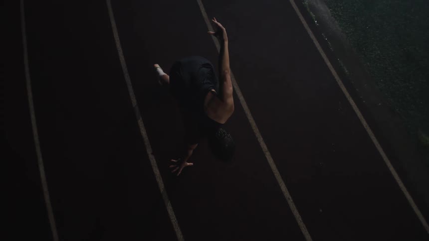 Man in long distance running stance on an athletics track at night