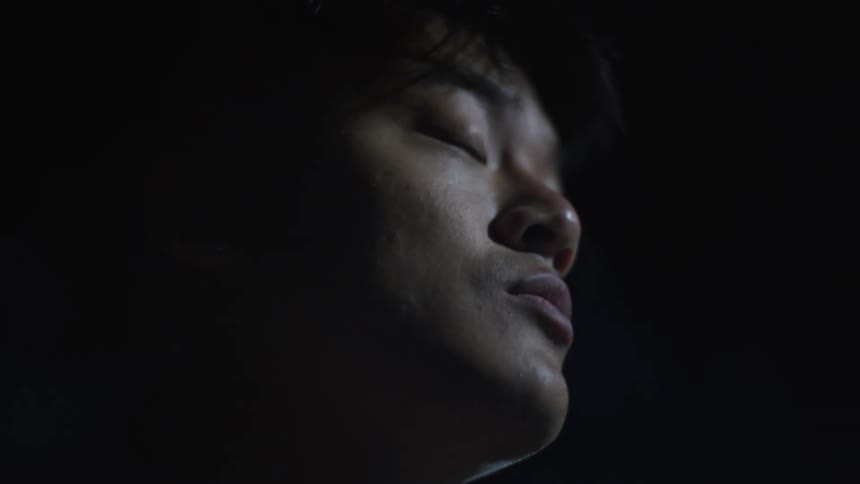 Fog blows past the face of an asian male standing outside at night