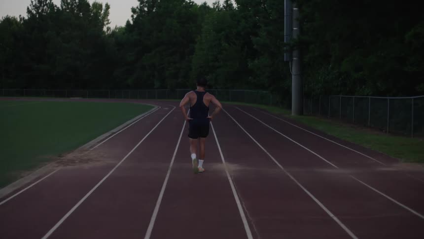 Back view of a man walking on a running track with his hands on his hips