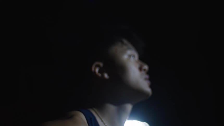 A man wearing a blue tank top is standing outside at night