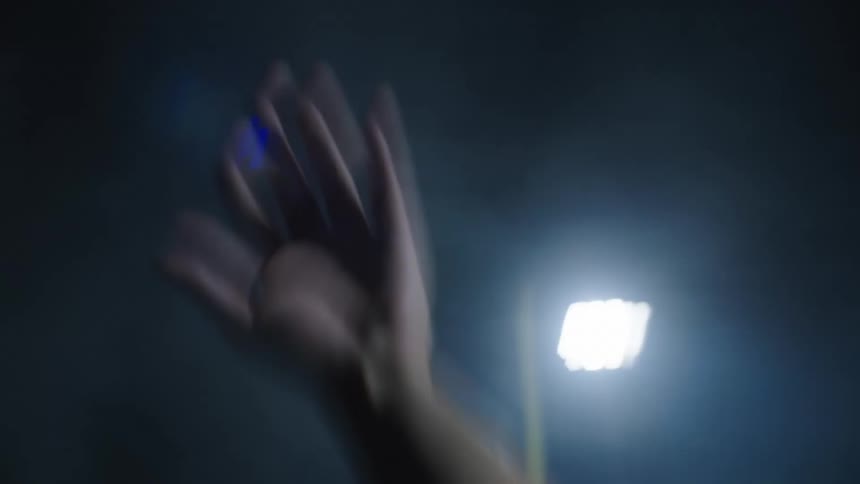 A male raises his hand while in a stadium at night