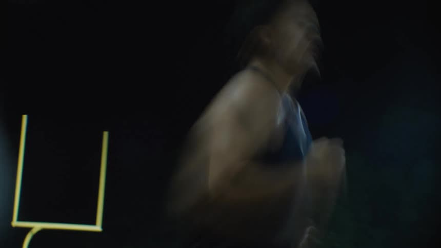 A man in a blue tank top is running fast on a running track at night