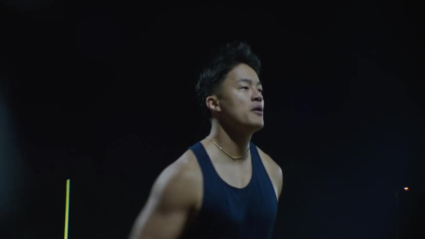 A young man in a blue tank top is running on a running track outdoors at night