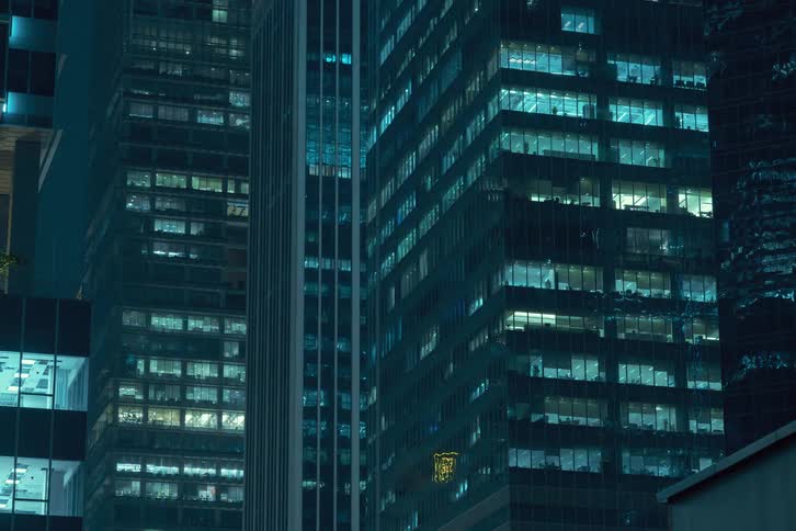 A cityscape at night featuring several tall office buildings with illuminated windows