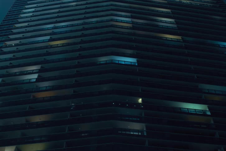 A closeup view of a multistory building at night with various windows illuminated creating patterns of lights