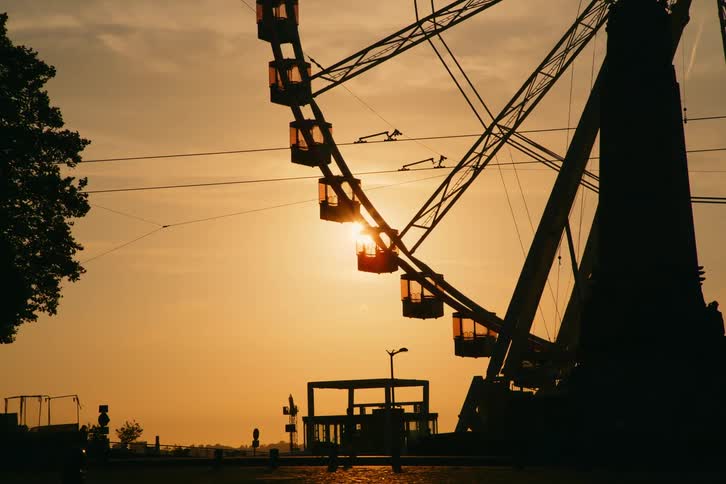 Silhouette of a ferris wheel spinning against an orange sunset sky