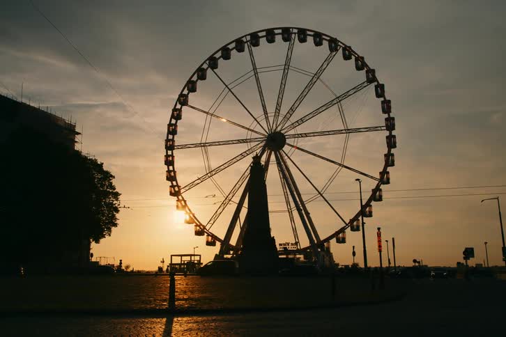 A silhouette of a ferris wheel that is rotating on a dark morning