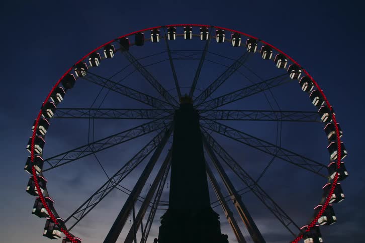 A roller coaster with red lights and white accents spinning against a twilight sky