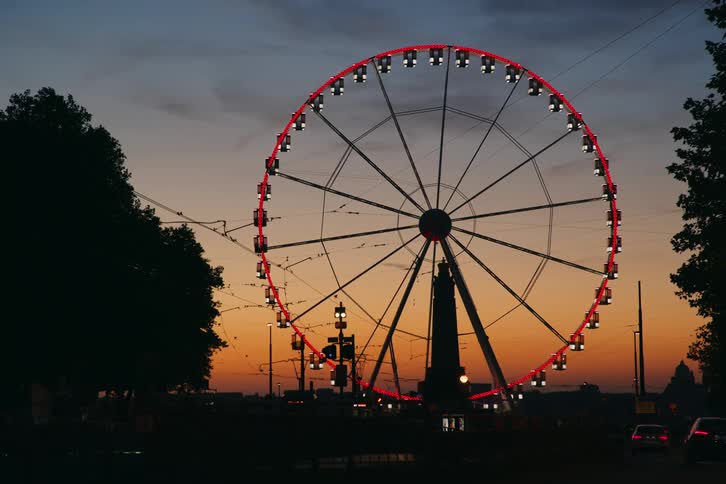 Traffic moves across roads near a brightly lit ferris wheel