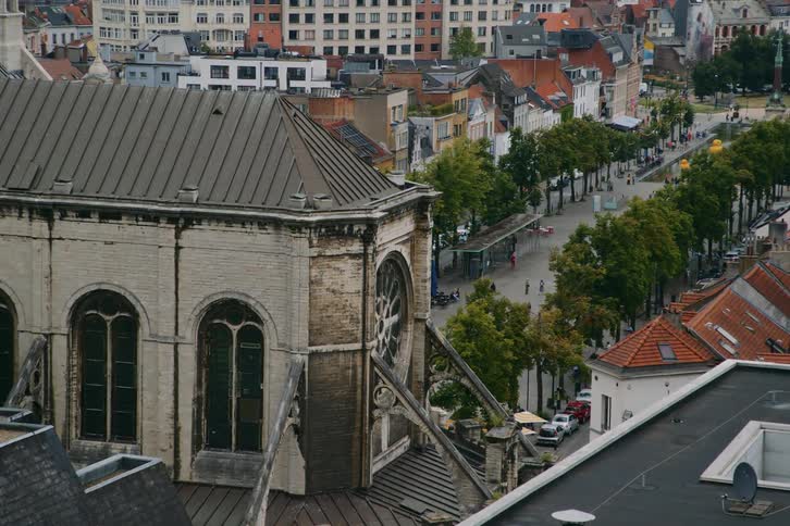 A city with several loads and a square with several trees of people and on the left side there is an old building