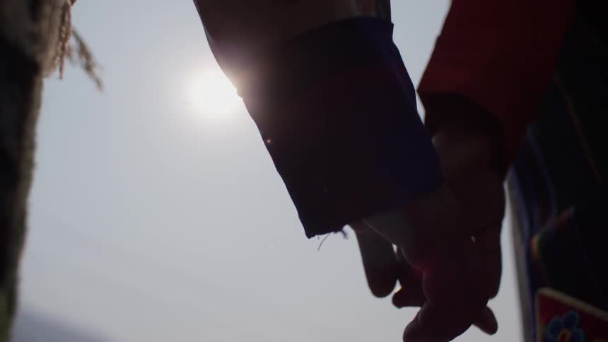 Closeup of two people holding hands with the sun in the background