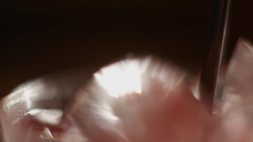 Closeup of a red liquid with ice cubes and a black straw being shaked
