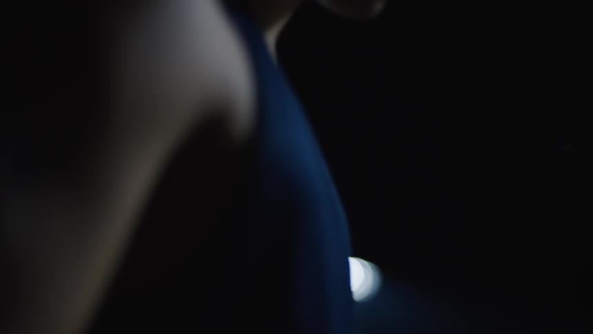 A man standing wearing a blue tank top and is in a dark environment