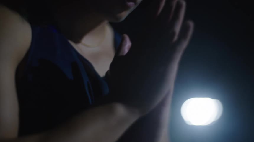 An asian male stands outdoors at night in fog and rubs his hands together